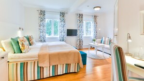 Un dormitorio con cama, televisor, escritorio con lámpara y ventana con cortinas.