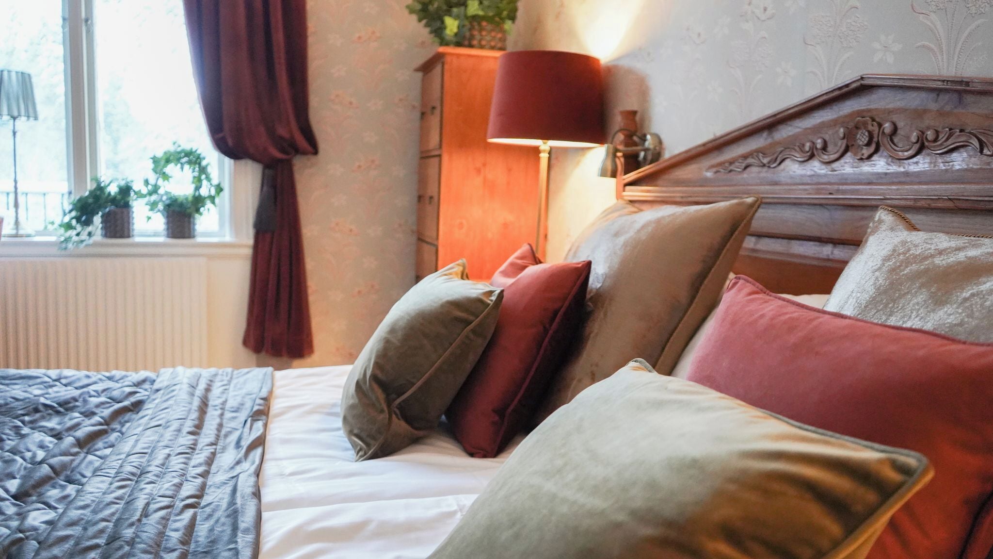 A neatly made bed with multiple pillows, a lamp, and a window with curtains.