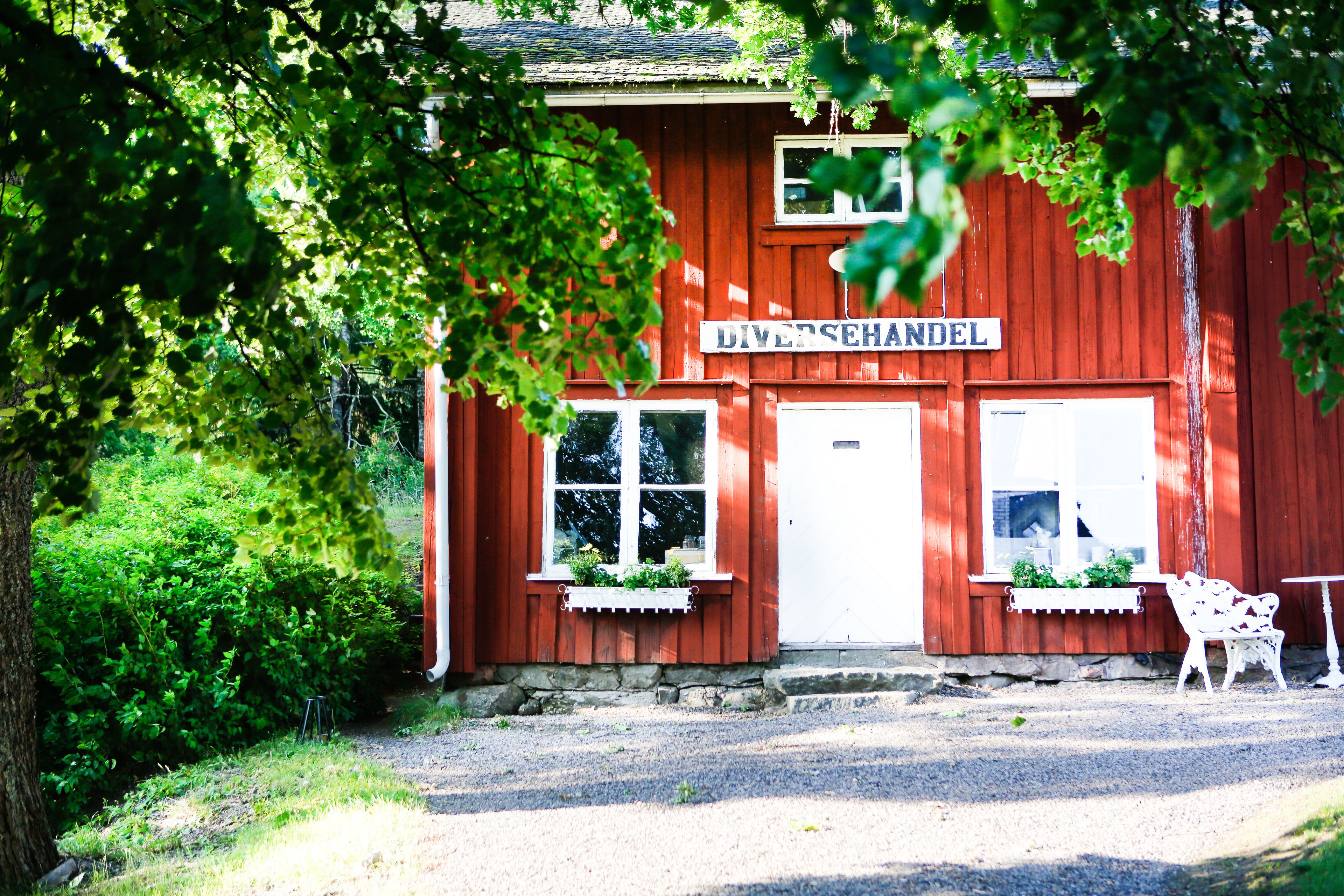 A red building with a sign reading "DIVERSSEHANDEL" and a white bench outside.