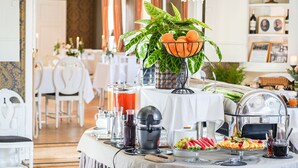 Un bufé de desayuno con diversas opciones de alimentos, un exprimidor y una planta decorativa.