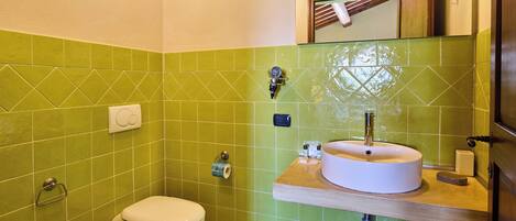 A bathroom with green tiles, a white toilet, a sink with a mirror above it, and a wooden countertop.