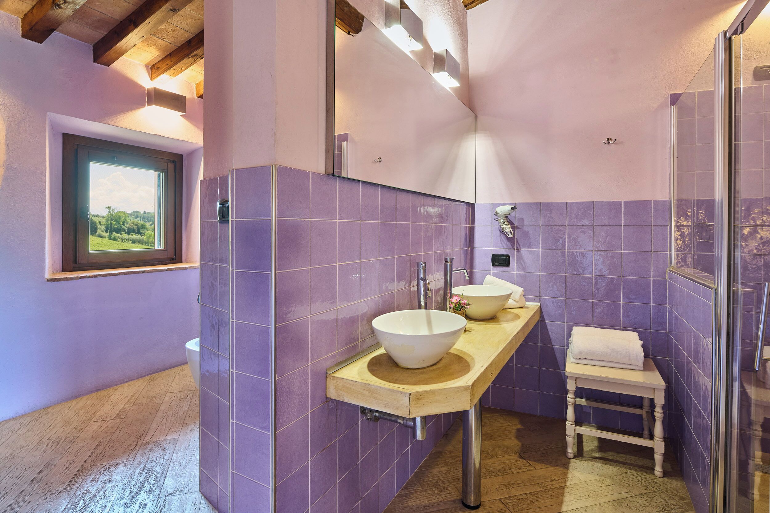 Une salle de bain avec des carreaux violets, un meuble-lavabo en bois, un grand miroir et une cabine de douche en verre.