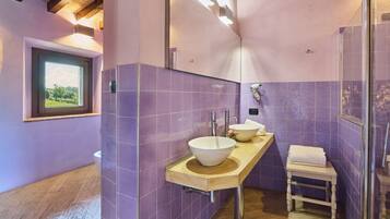 Une salle de bain avec des carreaux violets, un meuble-lavabo en bois, un grand miroir et une cabine de douche en verre.