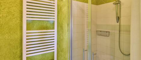 A bathroom with a glass shower enclosure, a white towel rack, and a tiled wall.