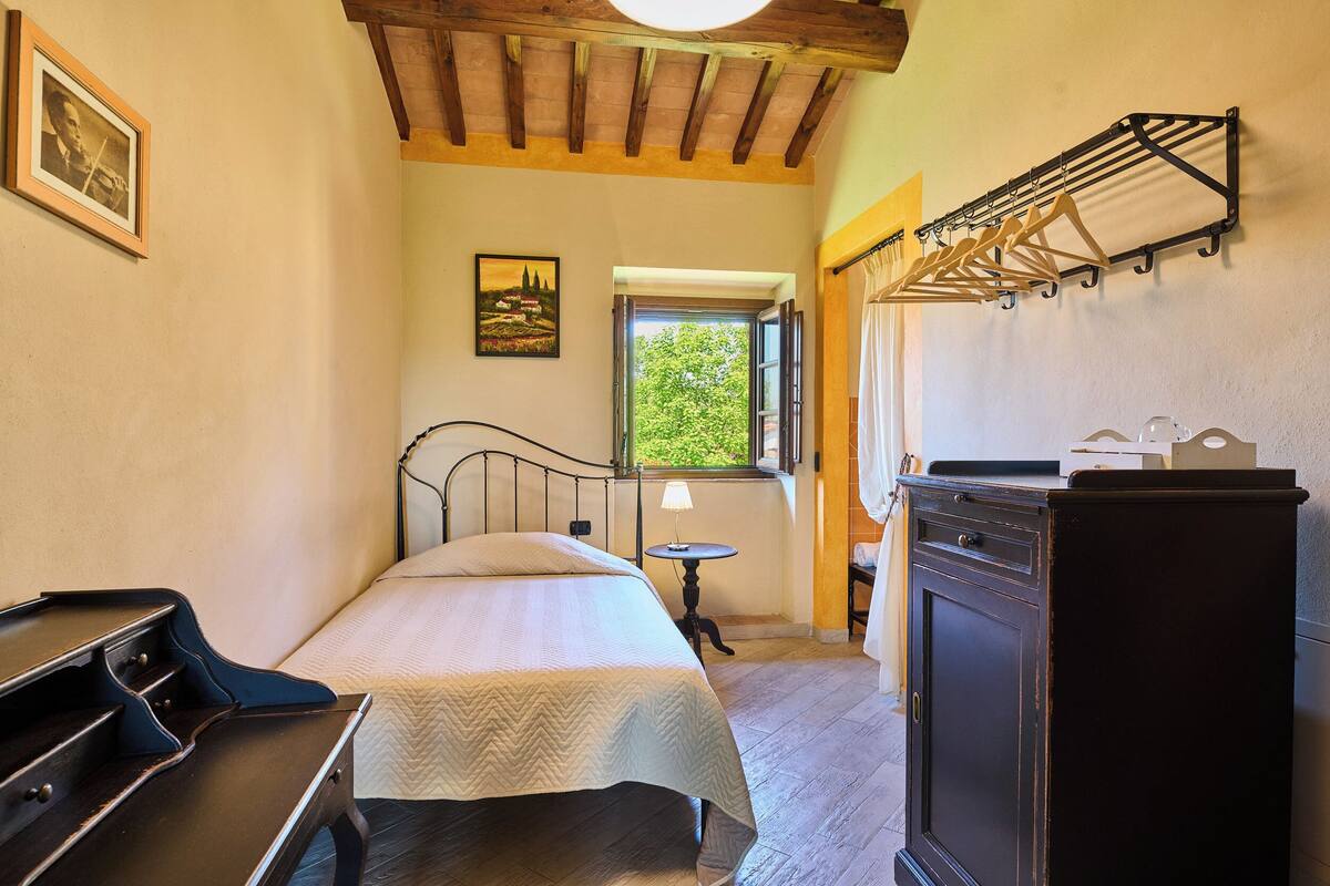 Une chambre à coucher comprenant un lit, une commode, une lampe et une fenêtre donnant sur un paysage verdoyant.