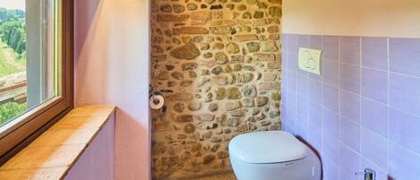 A bathroom with a stone wall, a toilet, a sink, and a window with a view of greenery.
