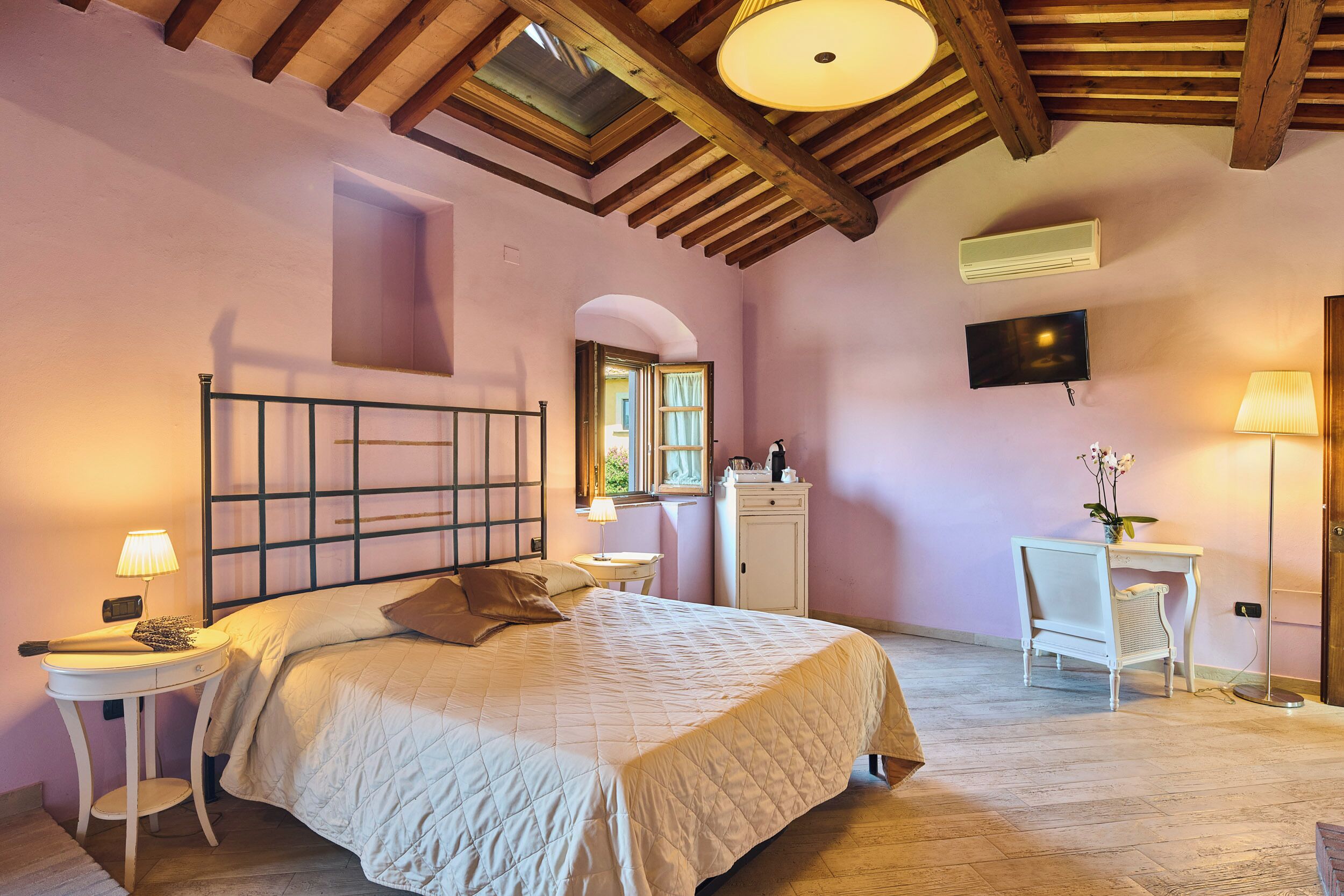 A bedroom with a bed, bedside tables, a desk, a chair, a TV, and a skylight.