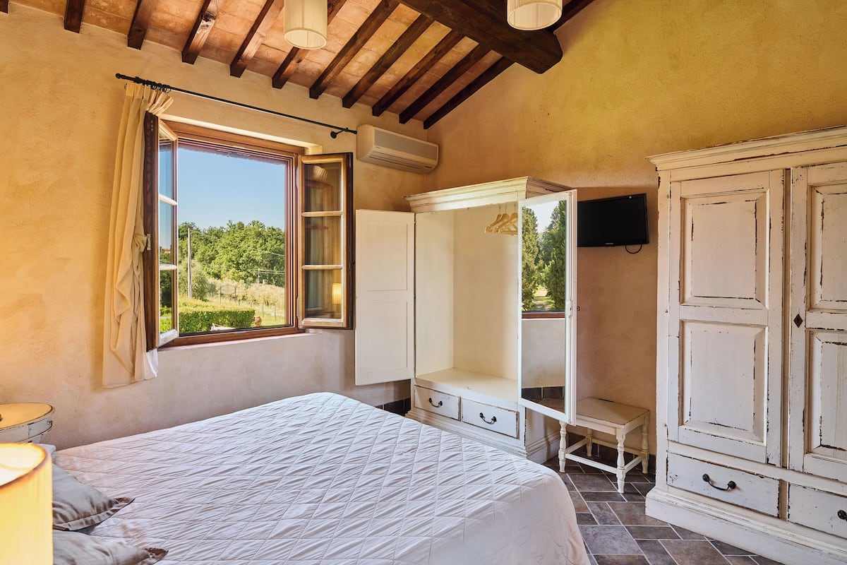 Une chambre à coucher avec un lit, une armoire, une télévision et une fenêtre avec des rideaux.