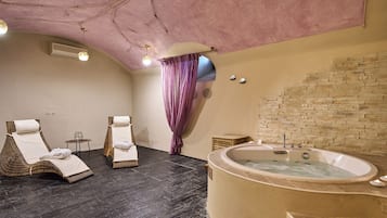 A spa room with two wicker chairs, a large freestanding bathtub, and a stone wall.