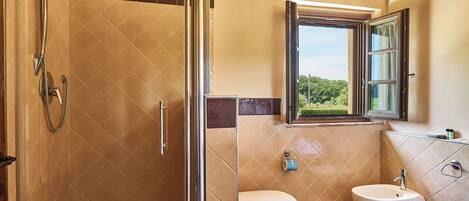 Une salle de bain équipée d’une douche, de toilettes, d’un bidet et d’une fenêtre donnant sur un espace verdoyant.