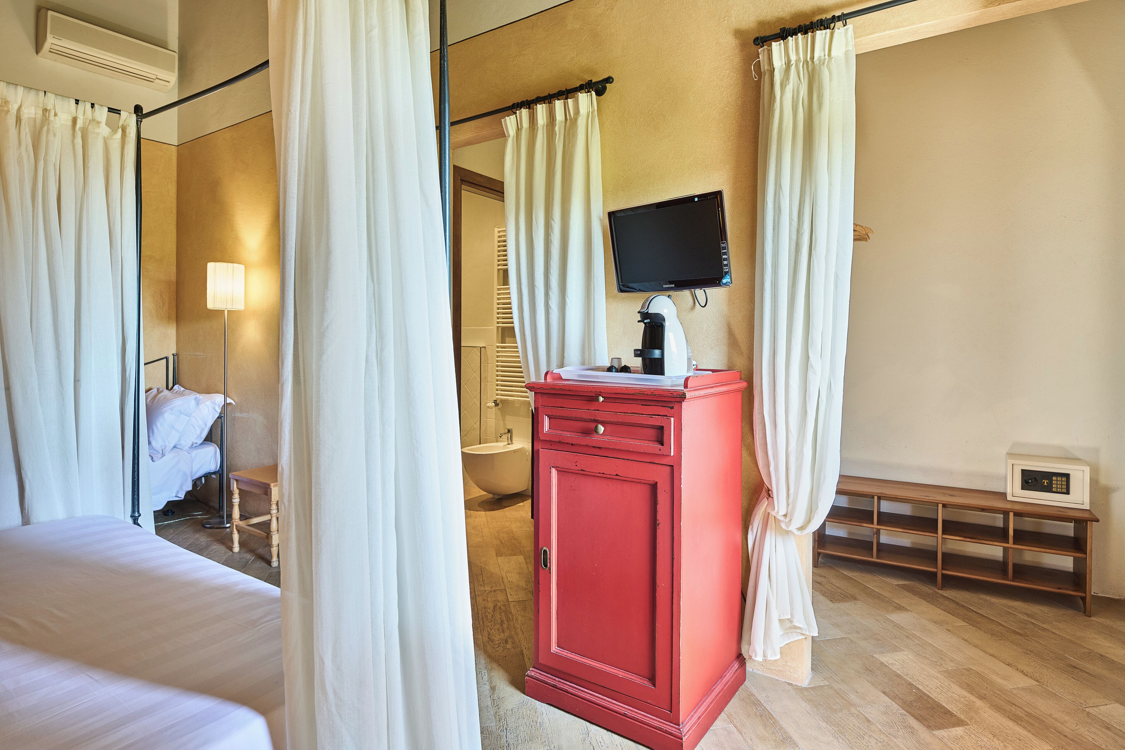 A hotel room with a bed, a red cabinet, a television, and a bedside table.