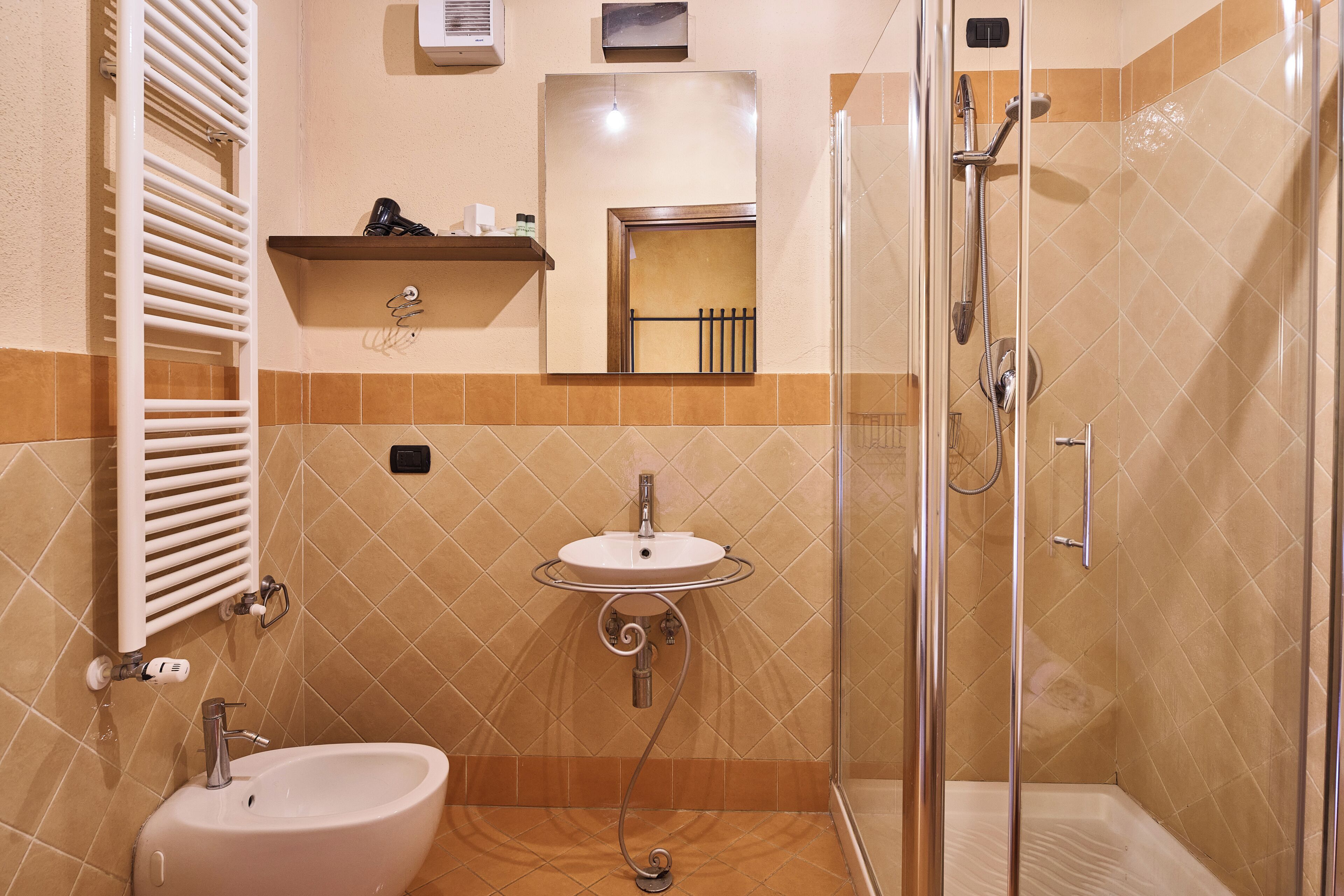 Un bagno con lavandino, specchio, porta asciugamani, doccia e termosifone.