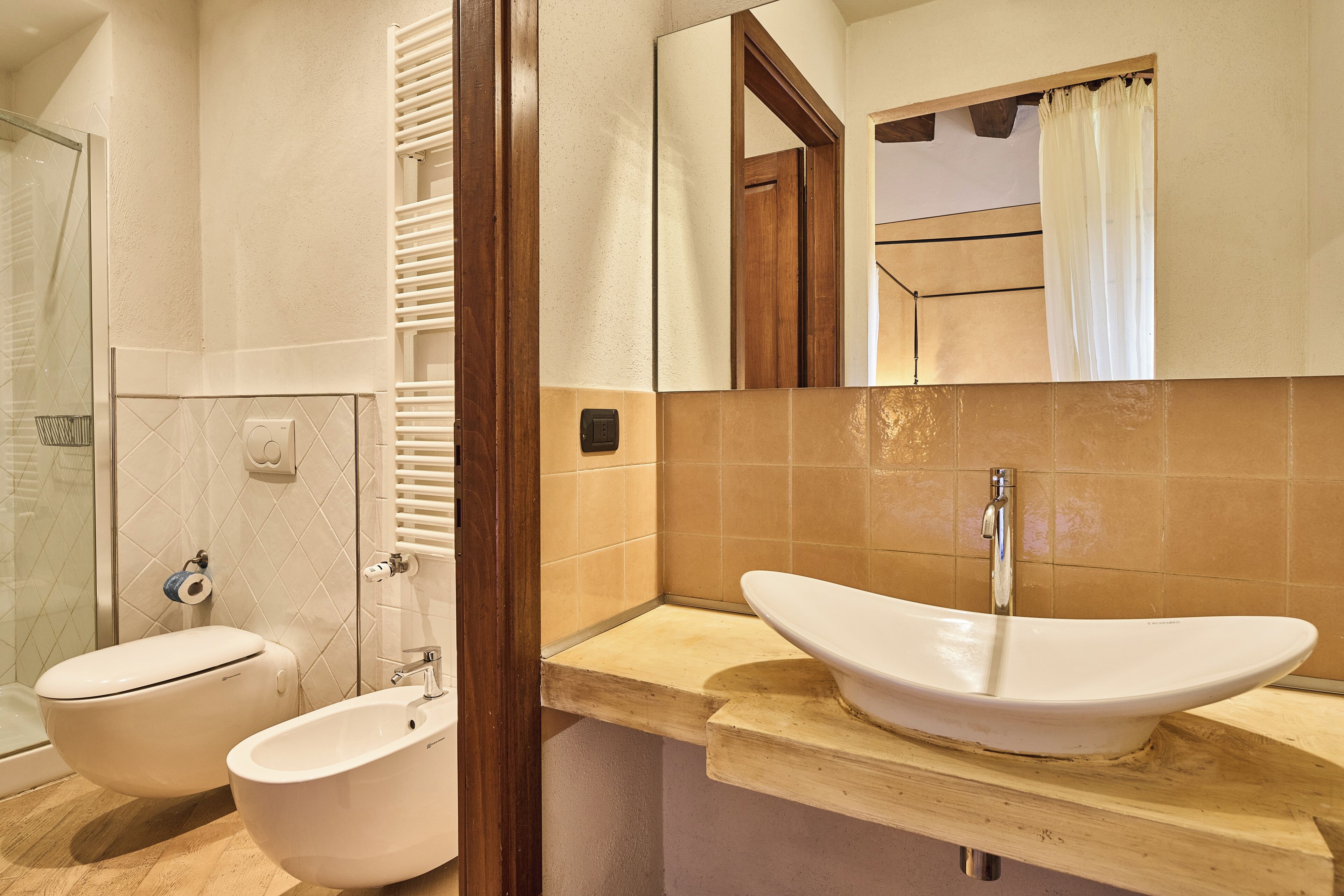 A bathroom with a white sink, two toilets, a shower, and a mirror.