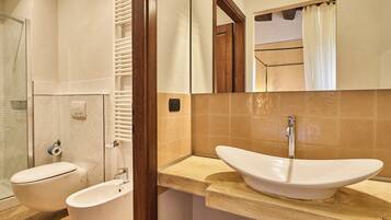 A bathroom with a white sink, two toilets, a shower, and a mirror.