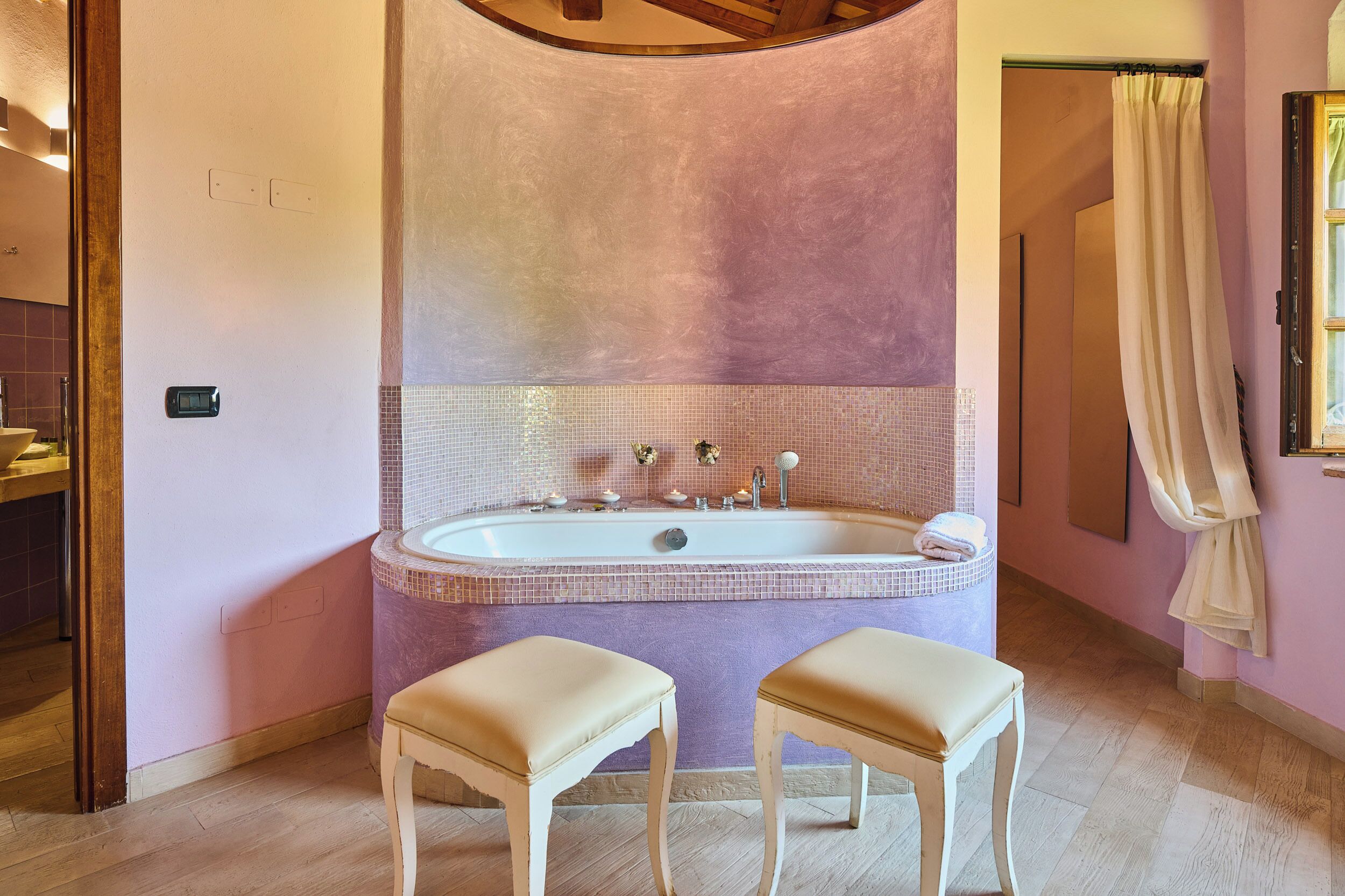 A bathroom with a large bathtub, two stools, and a mirror.