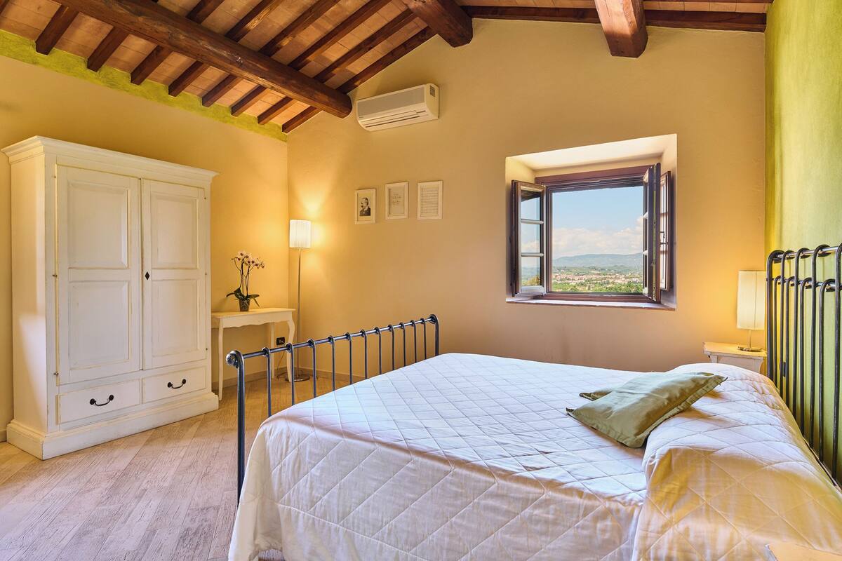 Une chambre à coucher avec un lit, une fenêtre donnant sur un beau paysage, une armoire et une table de chevet.