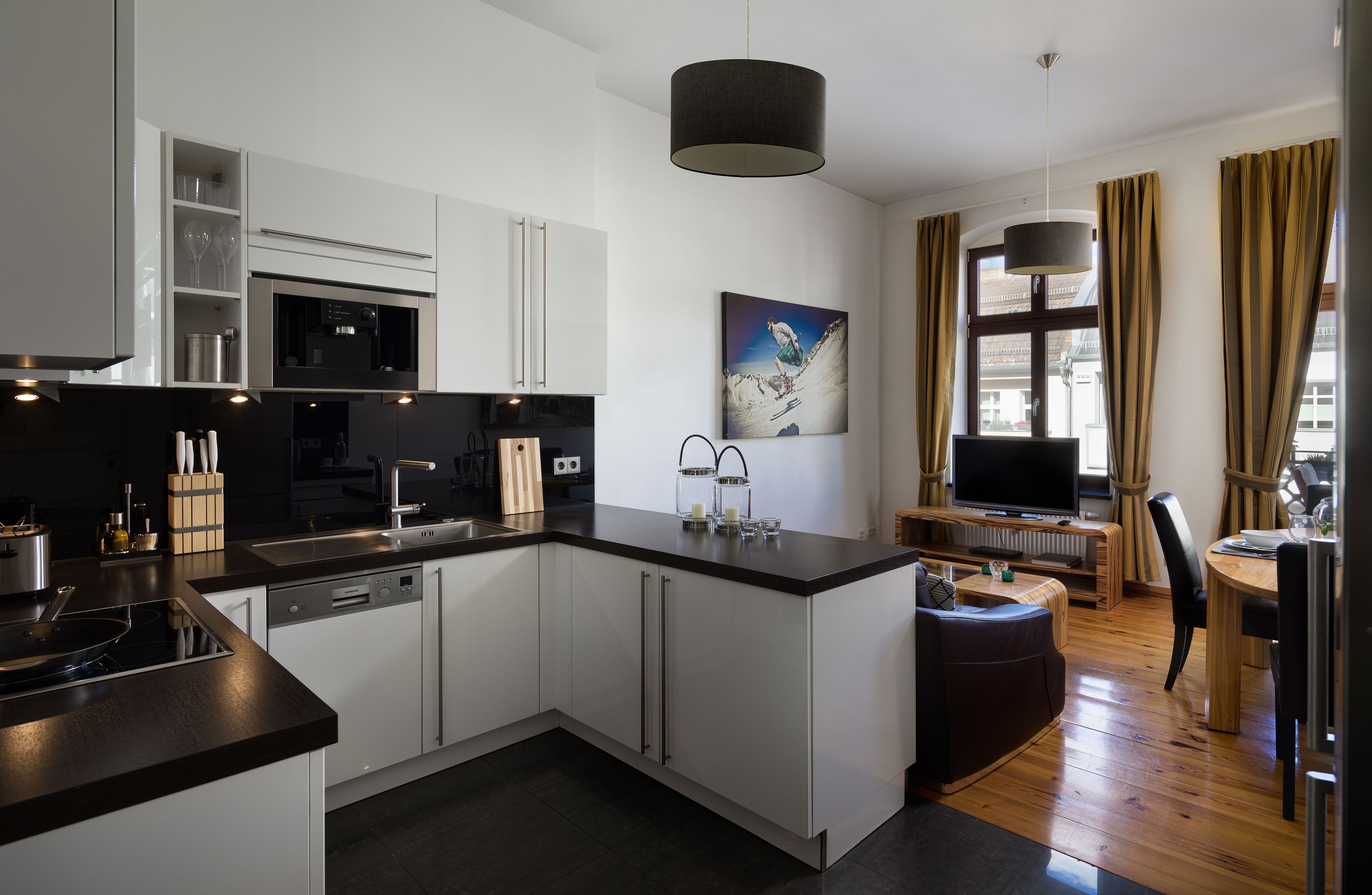 A modern kitchen with white cabinets, a black countertop, and a dining area with a wooden table and chairs.