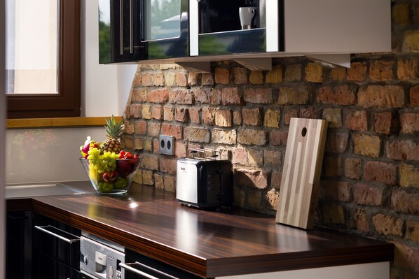 A kitchen with a brick wall, a wooden countertop, a fruit bowl, a toaster, and a cabinet above the counter. - Luxoise Apartments Berlin Friedrichshain (Berlin)