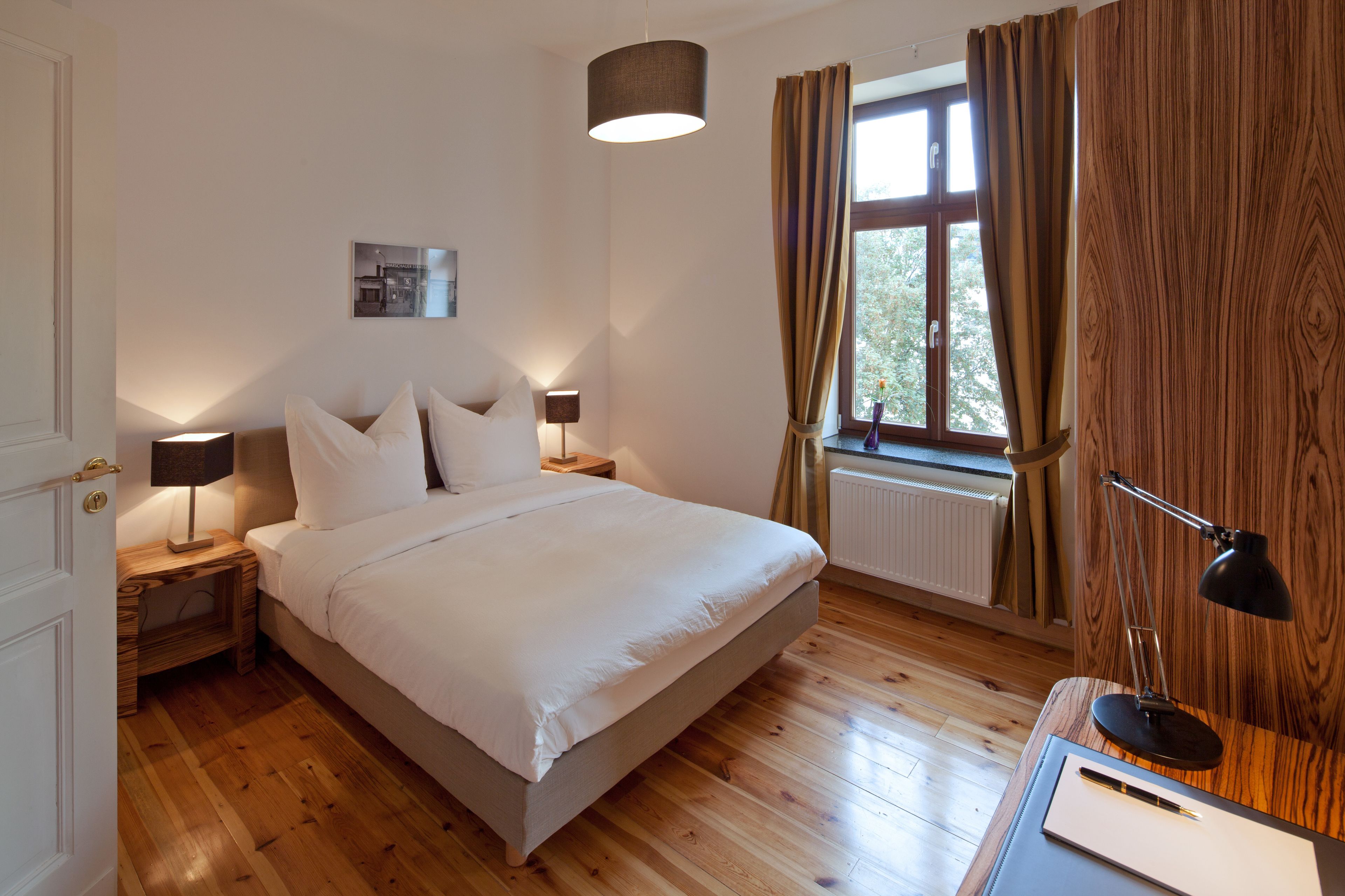 Une chambre à coucher avec un lit, des lampes de chevet, une fenêtre avec des rideaux et un radiateur.