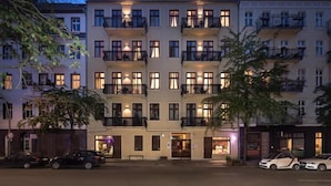 Een hotel met meerdere verdiepingen, balkons, een entree op de begane grond en geparkeerde auto's.