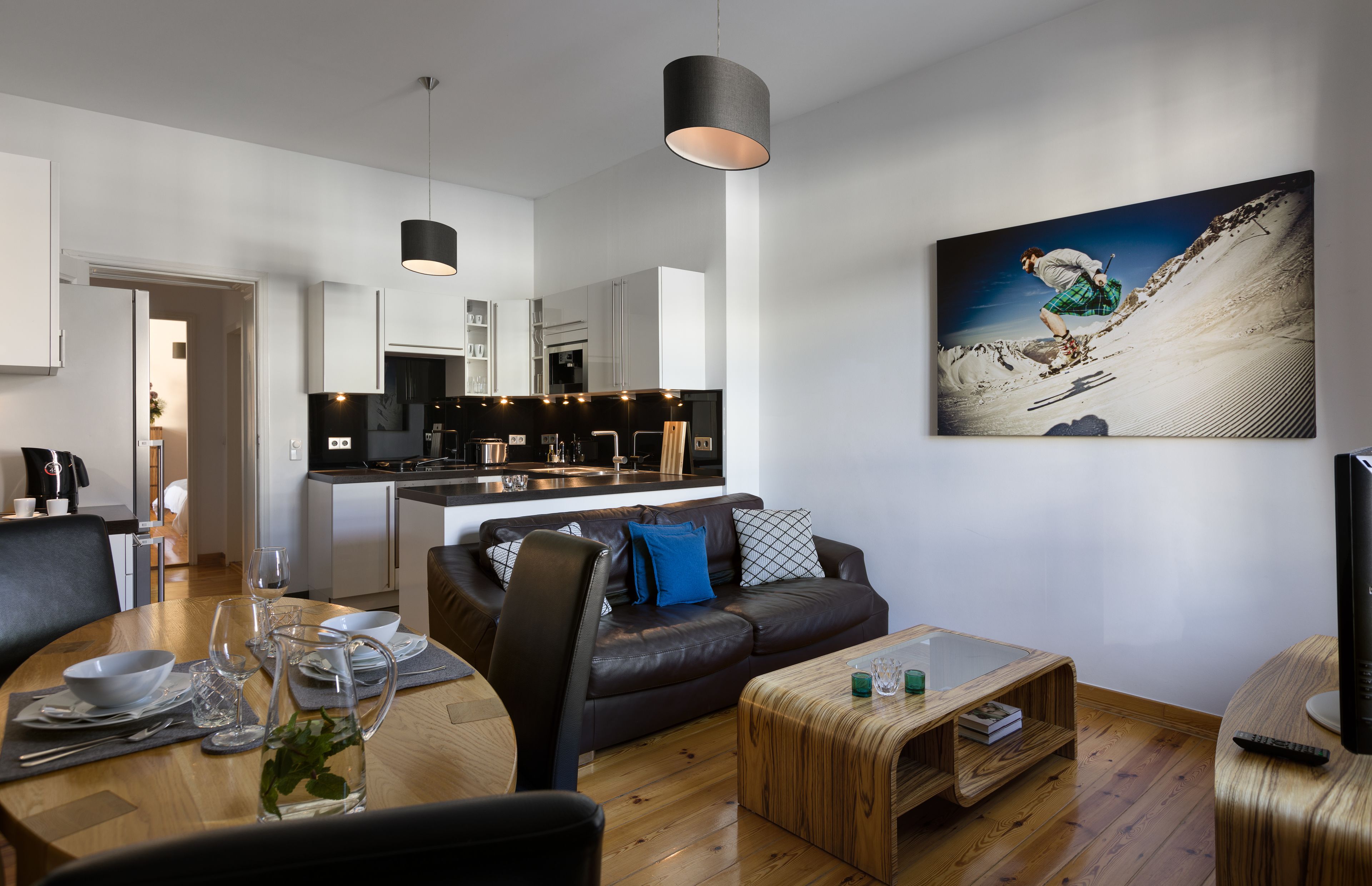 A modern living room with a brown leather sofa, a wooden coffee table, and a dining area with a glass table set for two.