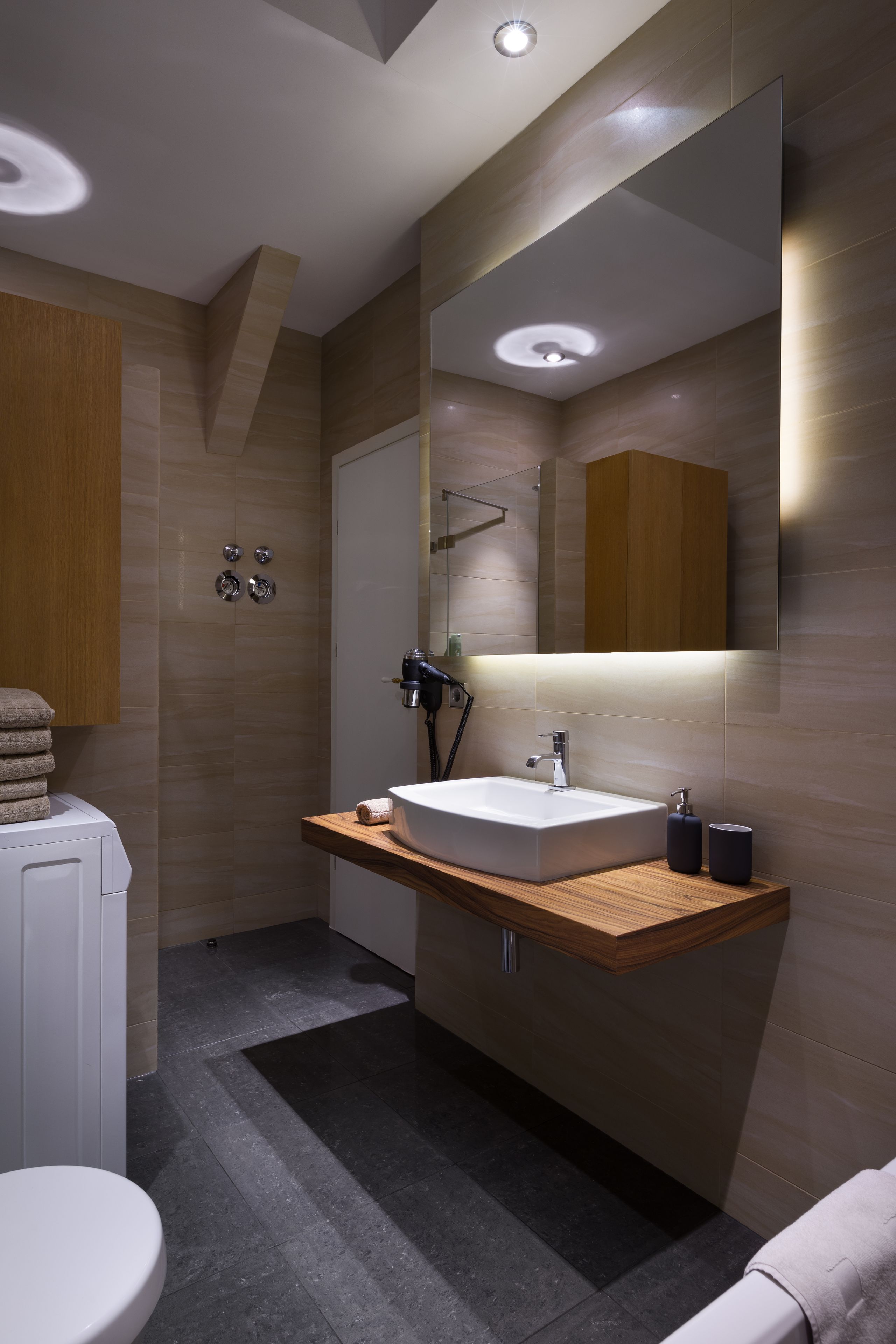A modern bathroom with a large mirror, a wooden vanity, a white sink, and a toilet.