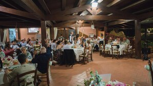 A covered outdoor dining area with multiple tables and chairs, wooden beams on the ceiling, and a stage with a performer. - Agriturismo Poggio Corbello (Massa Marittima)