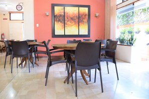 A dining area with a wooden table and black chairs, a large abstract painting on the wall, and a window with plants outside. - Murali Hostal Guayaquil (Guayaquil)