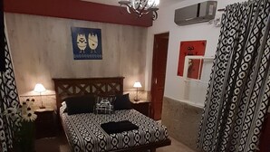 Un dormitorio con cama, lámparas de noche, una araña, cómoda y cortinas estampadas.