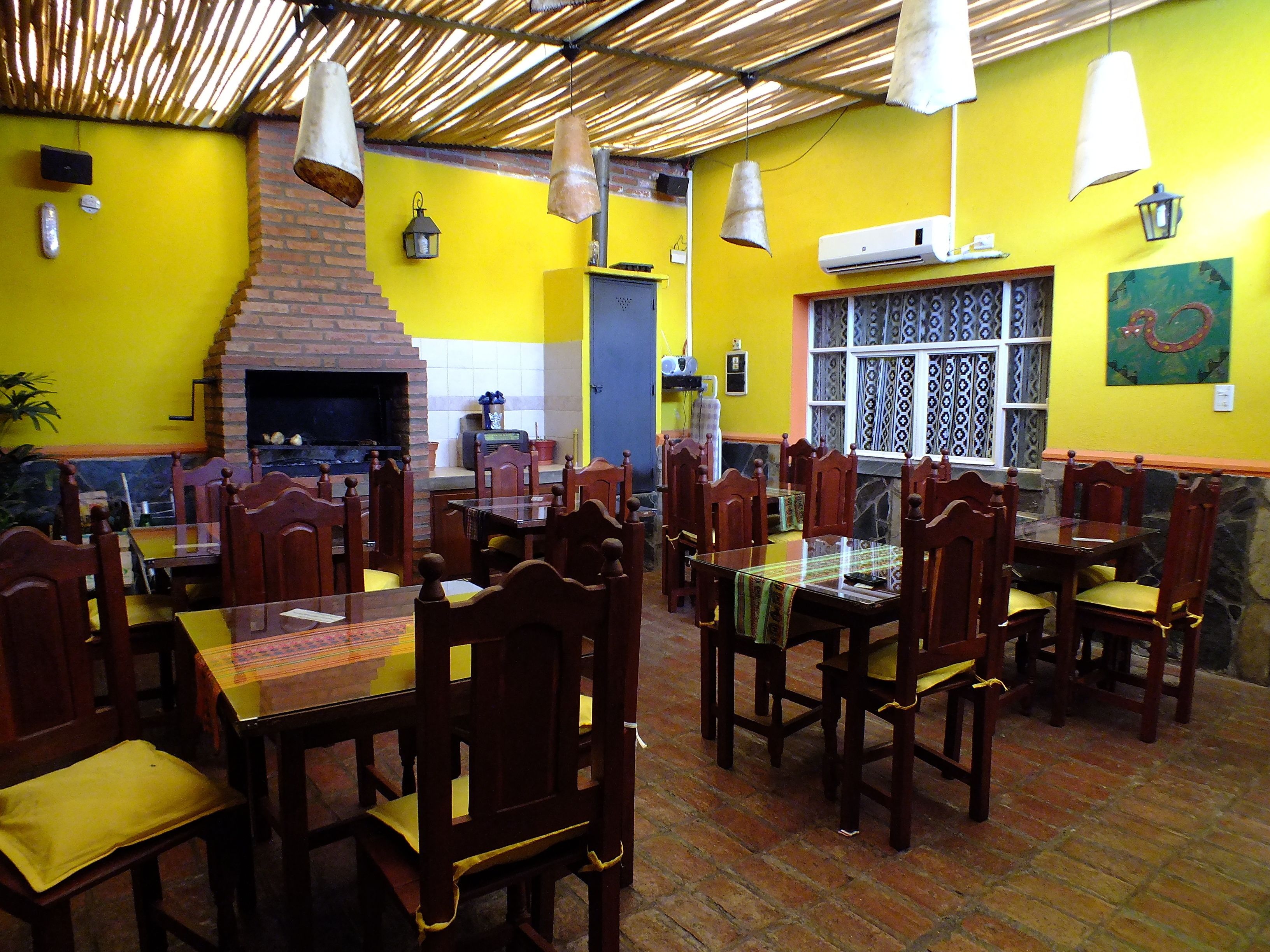 Un restaurante con mesas y sillas de madera, una chimenea de ladrillo y paredes amarillas.