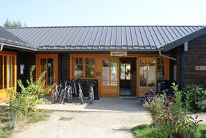 A wooden building with a metal roof, a reception area, and bicycles parked outside. - Le Village des Monédières - Slowmoov (Chamberet)
