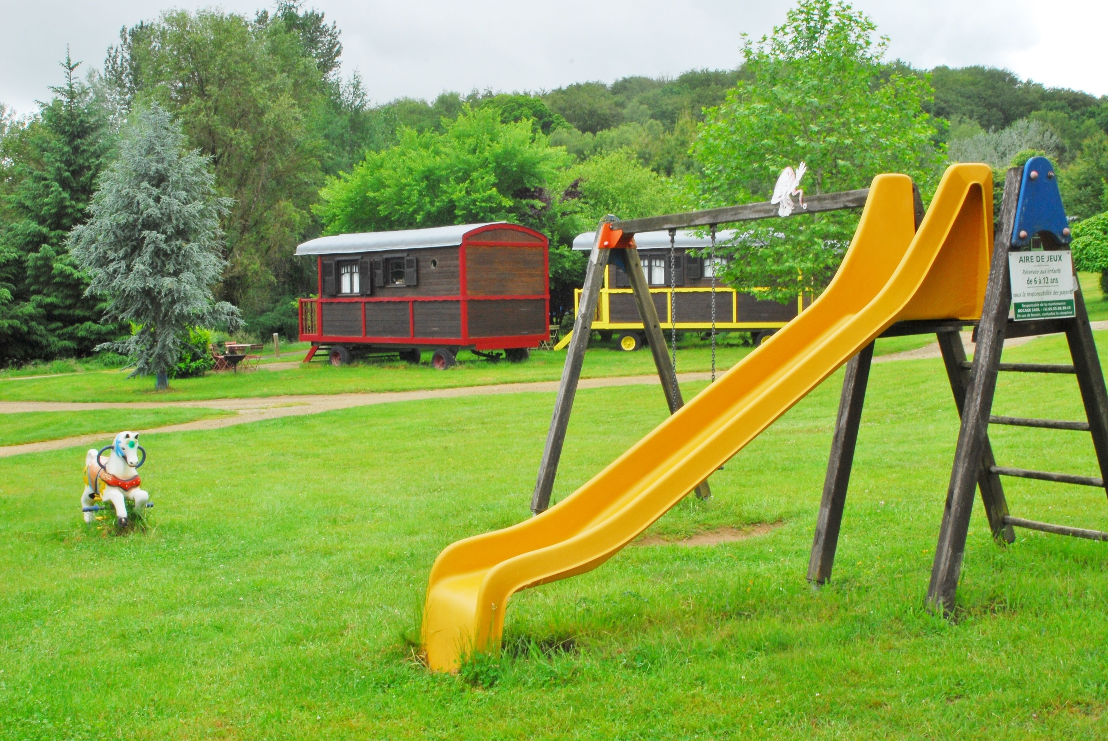 A playground with a yellow slide, a red and yellow play structure, and a small statue of a horse.