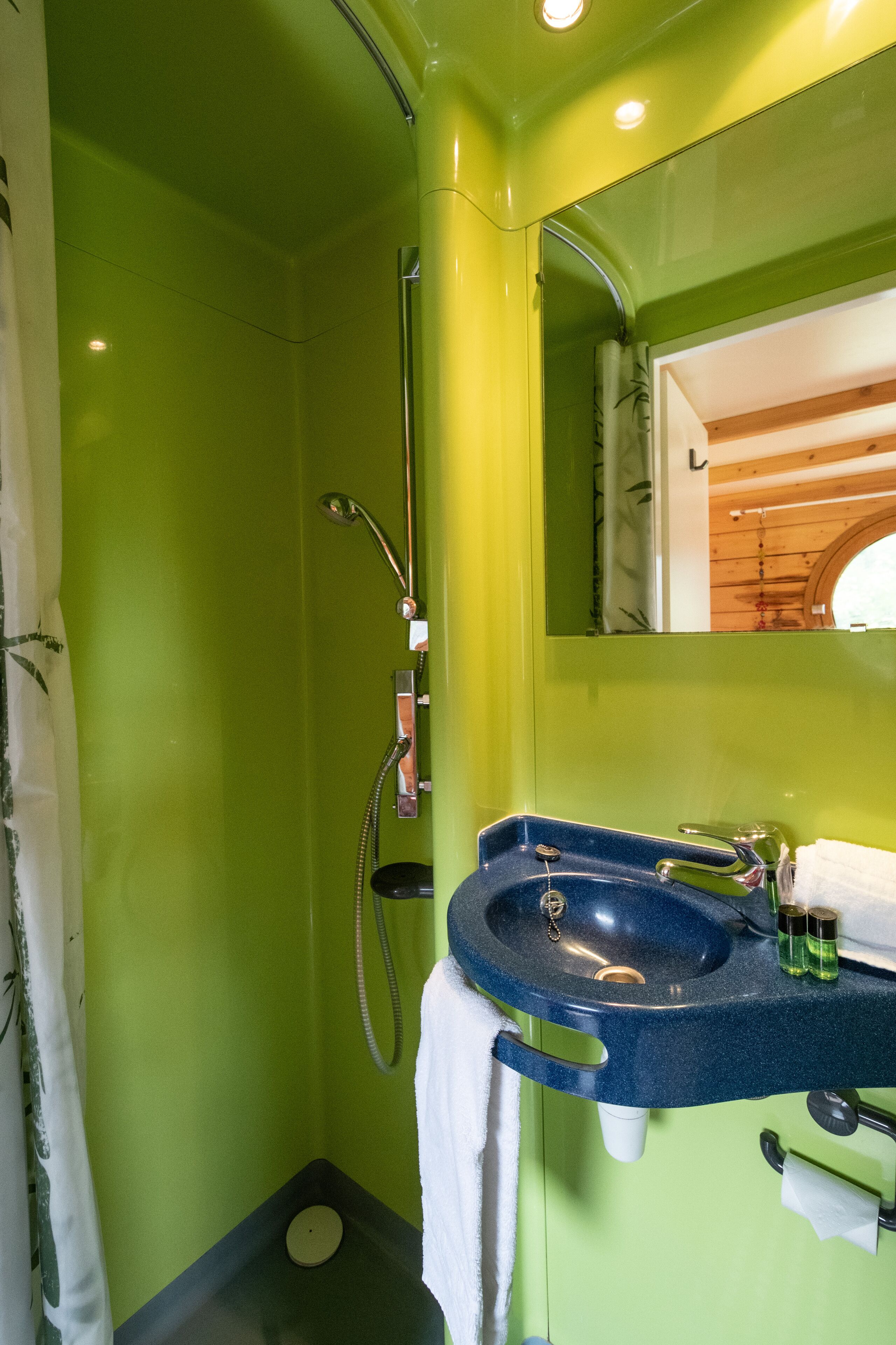 A bathroom with a green wall, a blue sink, a shower, and a mirror.