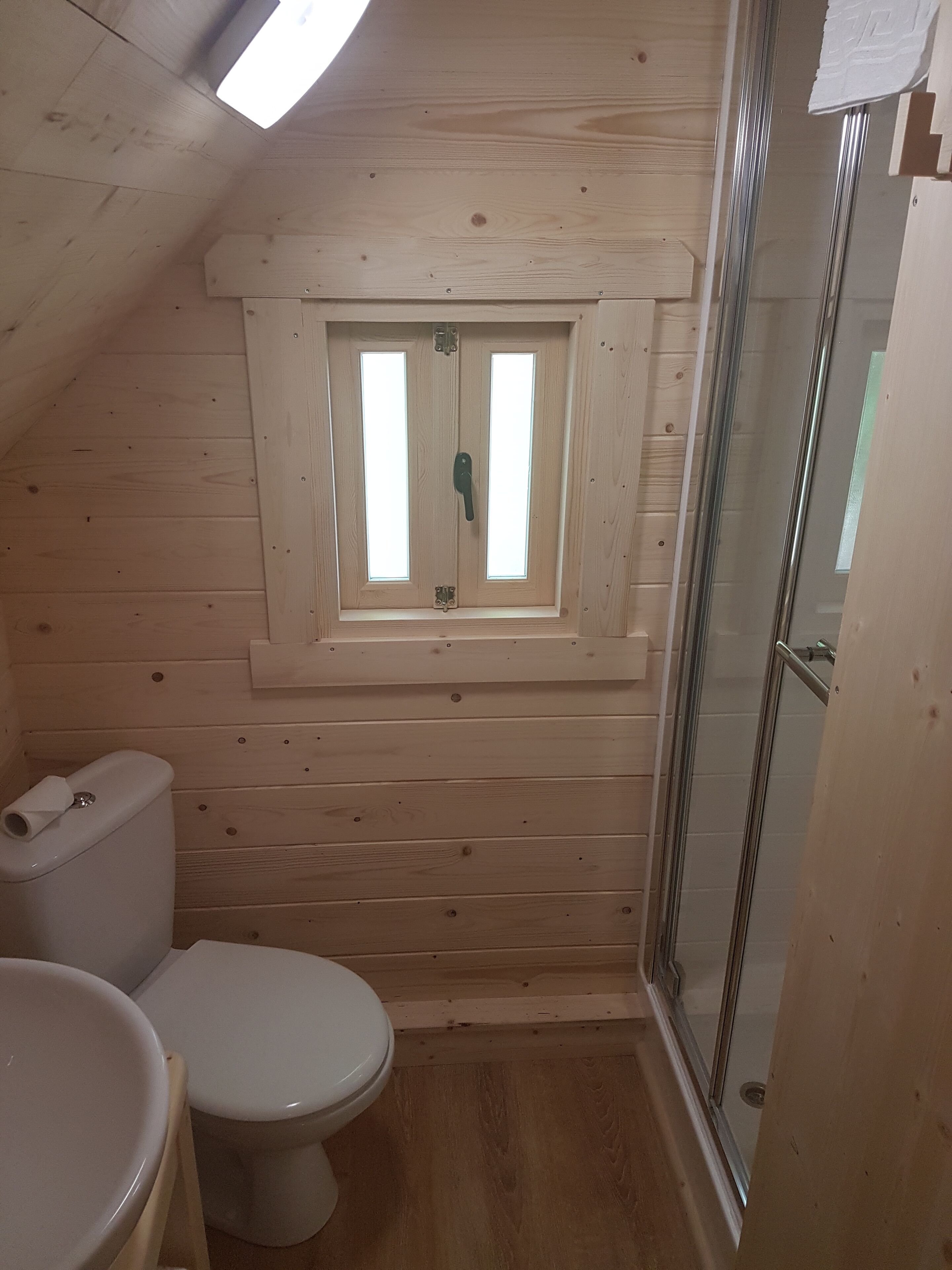 Ein kleines Badezimmer mit Holzvertäfelung, einem Oberlicht, einer Toilette und einer Dusche.