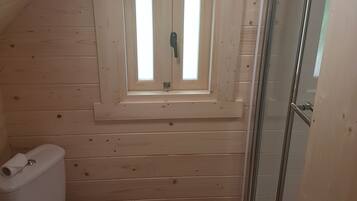 Ein kleines Badezimmer mit Holzvertäfelung, einem Oberlicht, einer Toilette und einer Dusche.