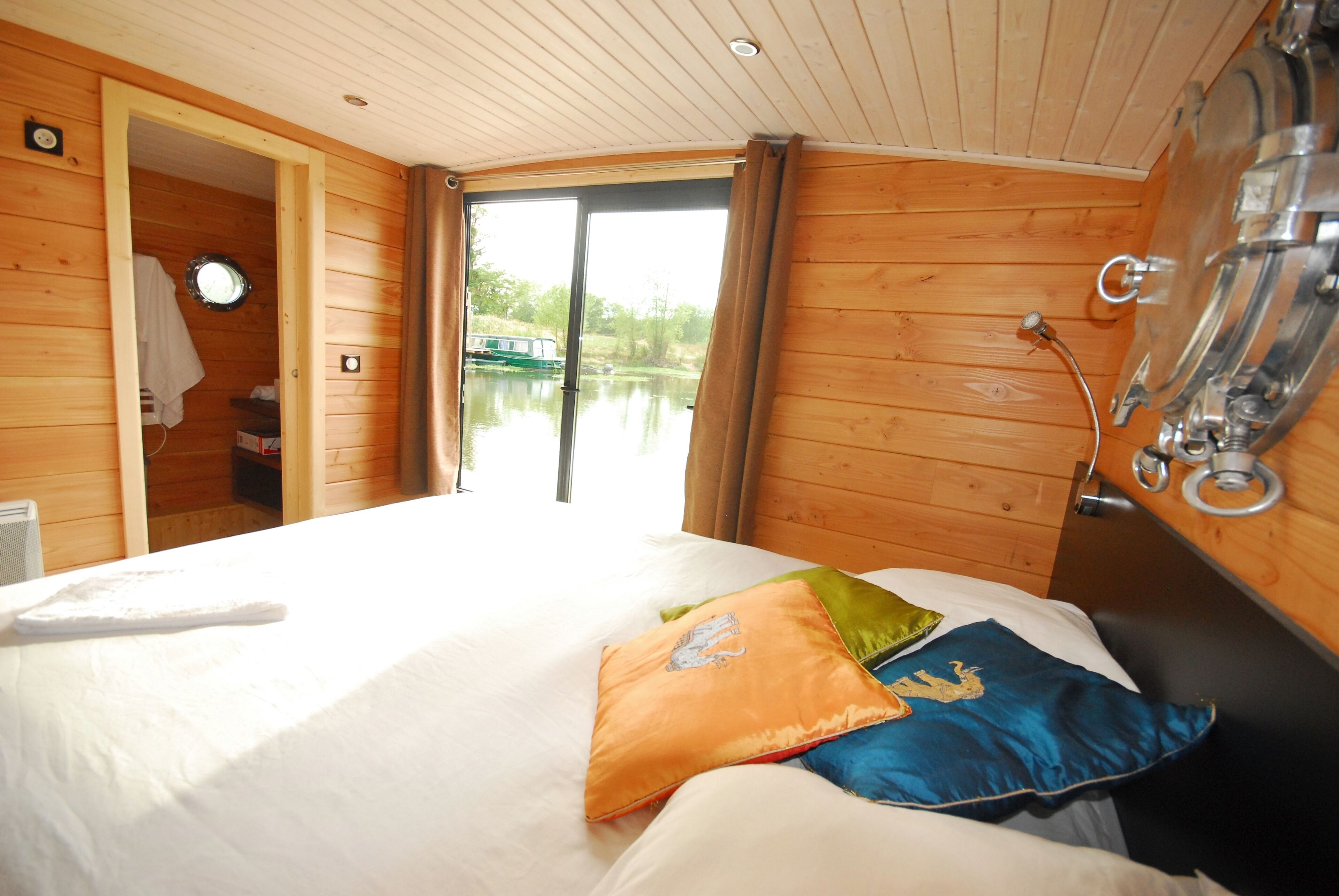 A wooden cabin room with a bed, a window, and a door leading to a bathroom.