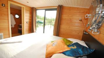A wooden cabin room with a bed, a window, and a door leading to a bathroom.