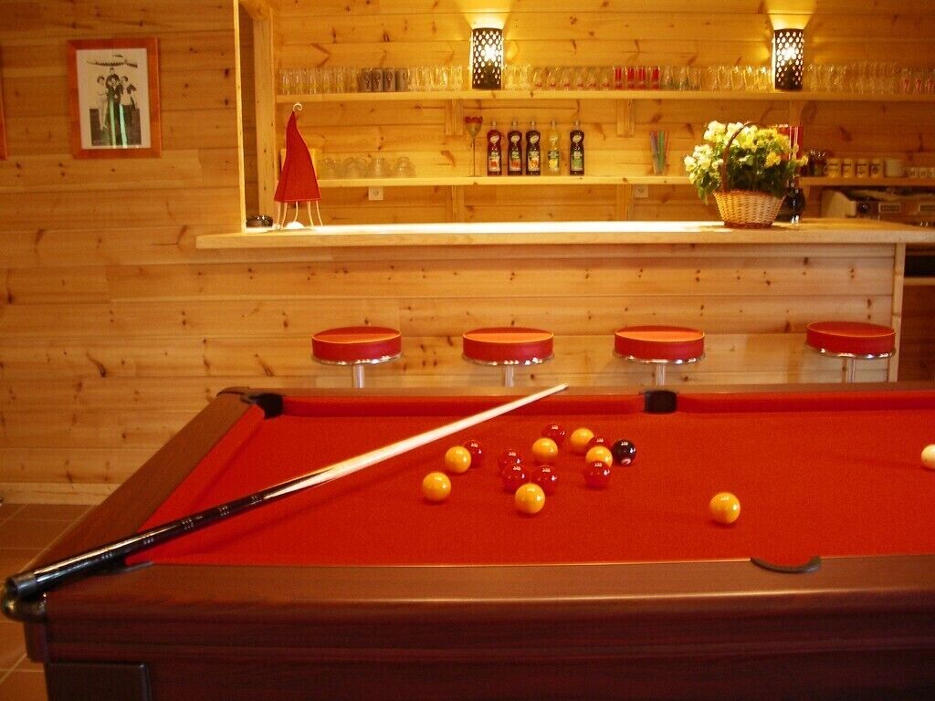 A pool table with balls, a pool cue, and a bar area with glasses and bottles.