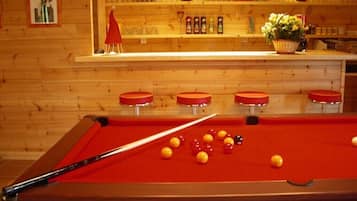 A pool table with balls, a pool cue, and a bar area with glasses and bottles.