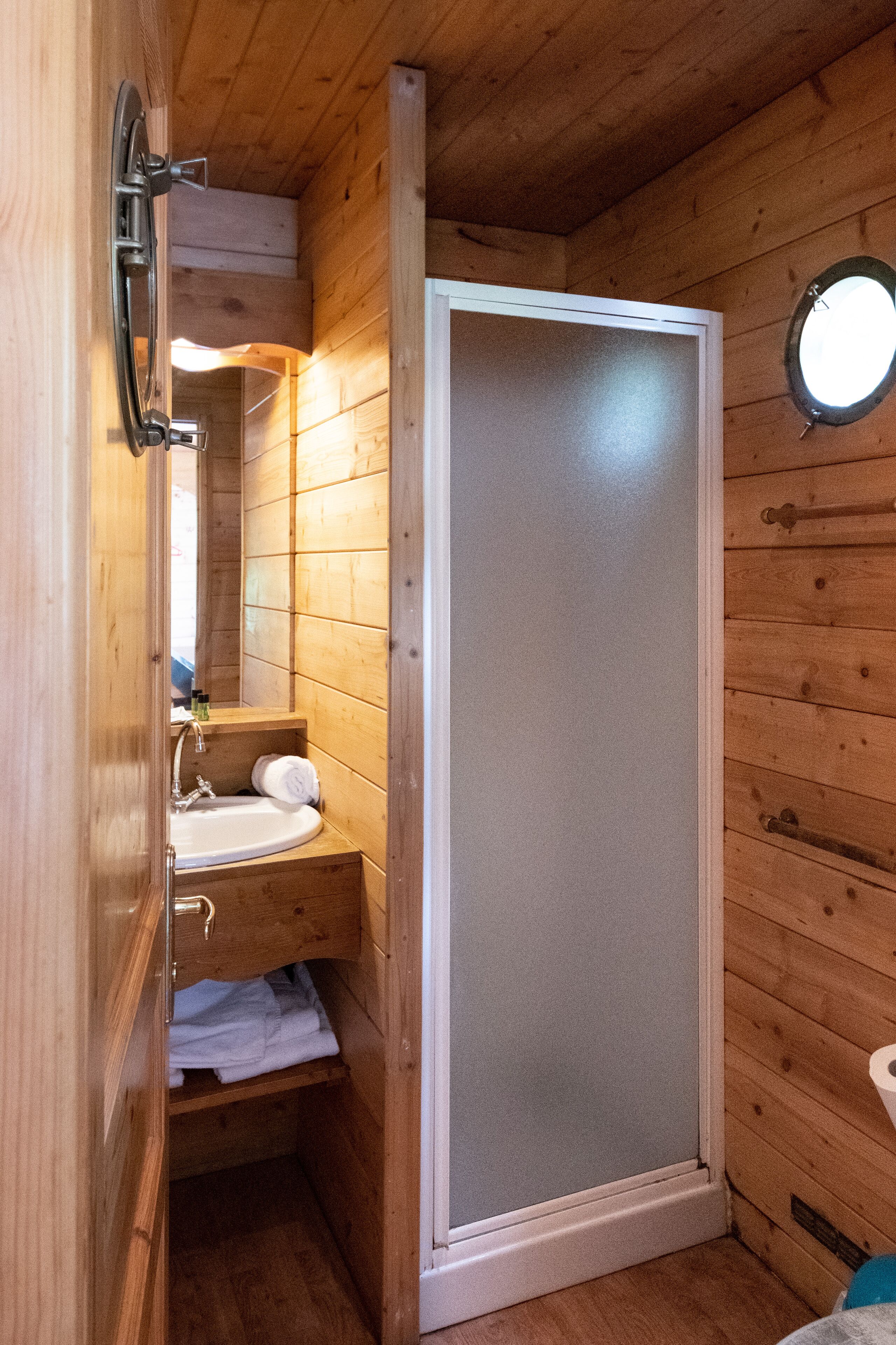 A wooden cabin bathroom with a shower, sink, and mirror.
