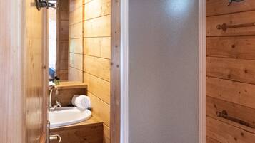 A wooden cabin bathroom with a shower, sink, and mirror.