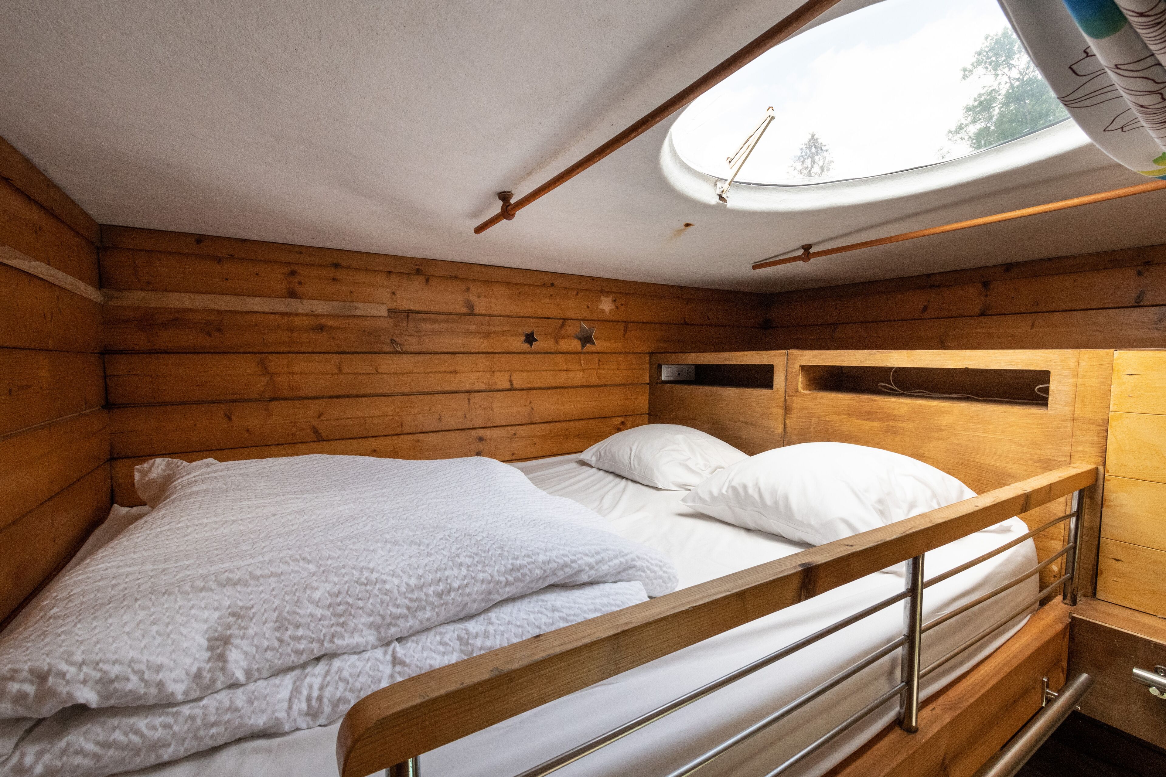 A wooden cabin room with a bunk bed, a skylight, and a small window.
