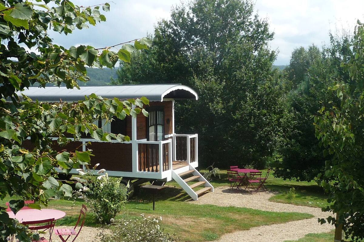 Eine kleine, eingeschossige Hütte mit einem Balkon, umgeben von einem Garten mit Tisch und Stühlen.