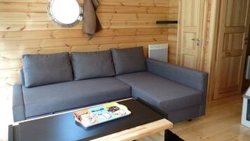 Interior moderno de una cabaña de troncos con un sofá seccional gris, una mesa de madera con un juego de mesa, un espejo redondo y una puerta.