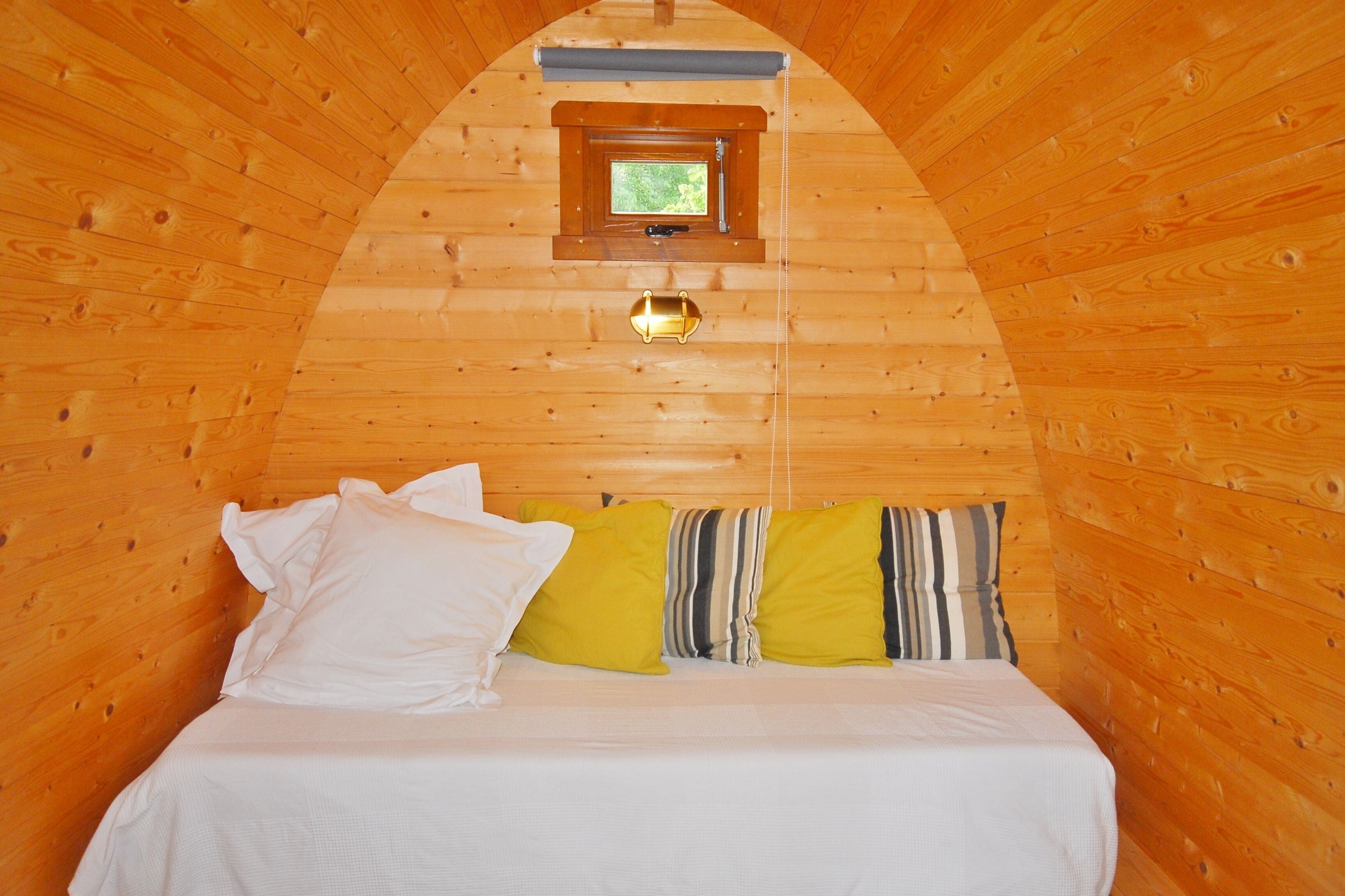 A cozy wooden cabin room with a bed, pillows, and a small window.
