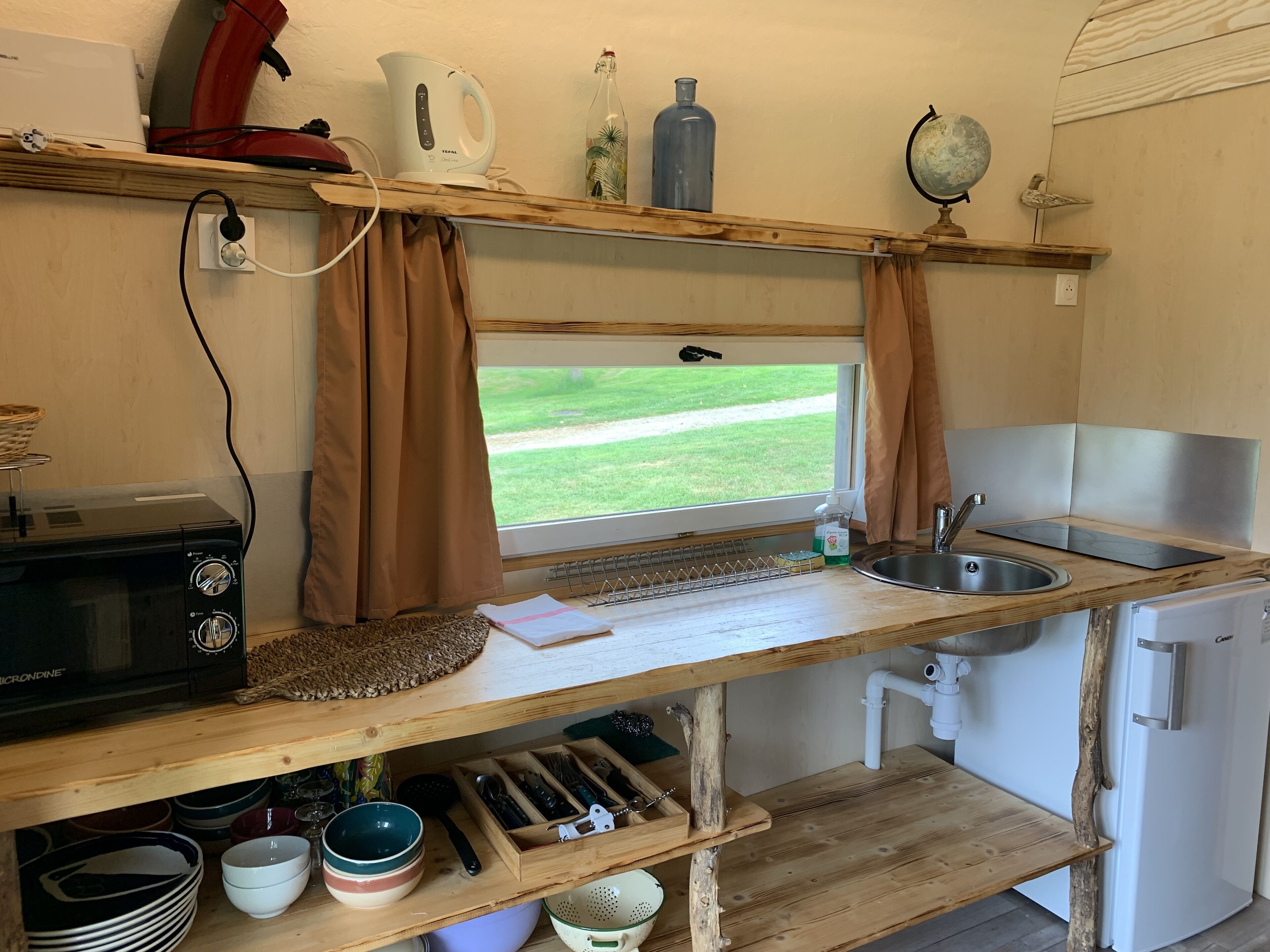 A compact kitchen with a window, a microwave, a sink, and a refrigerator.