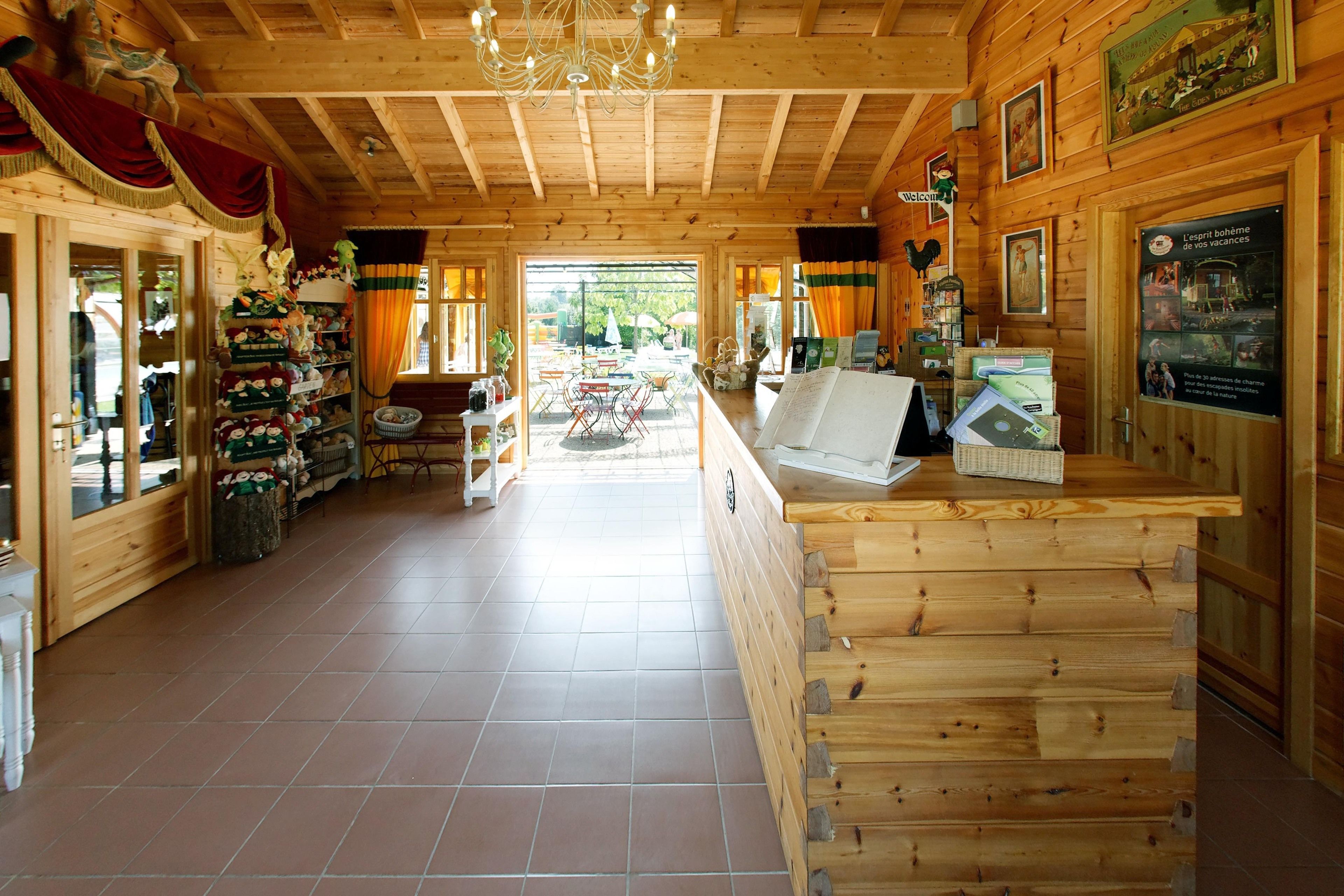 Een houten interieur met een receptiebalie, betegelde vloer en uitzicht op een buitenruimte.
