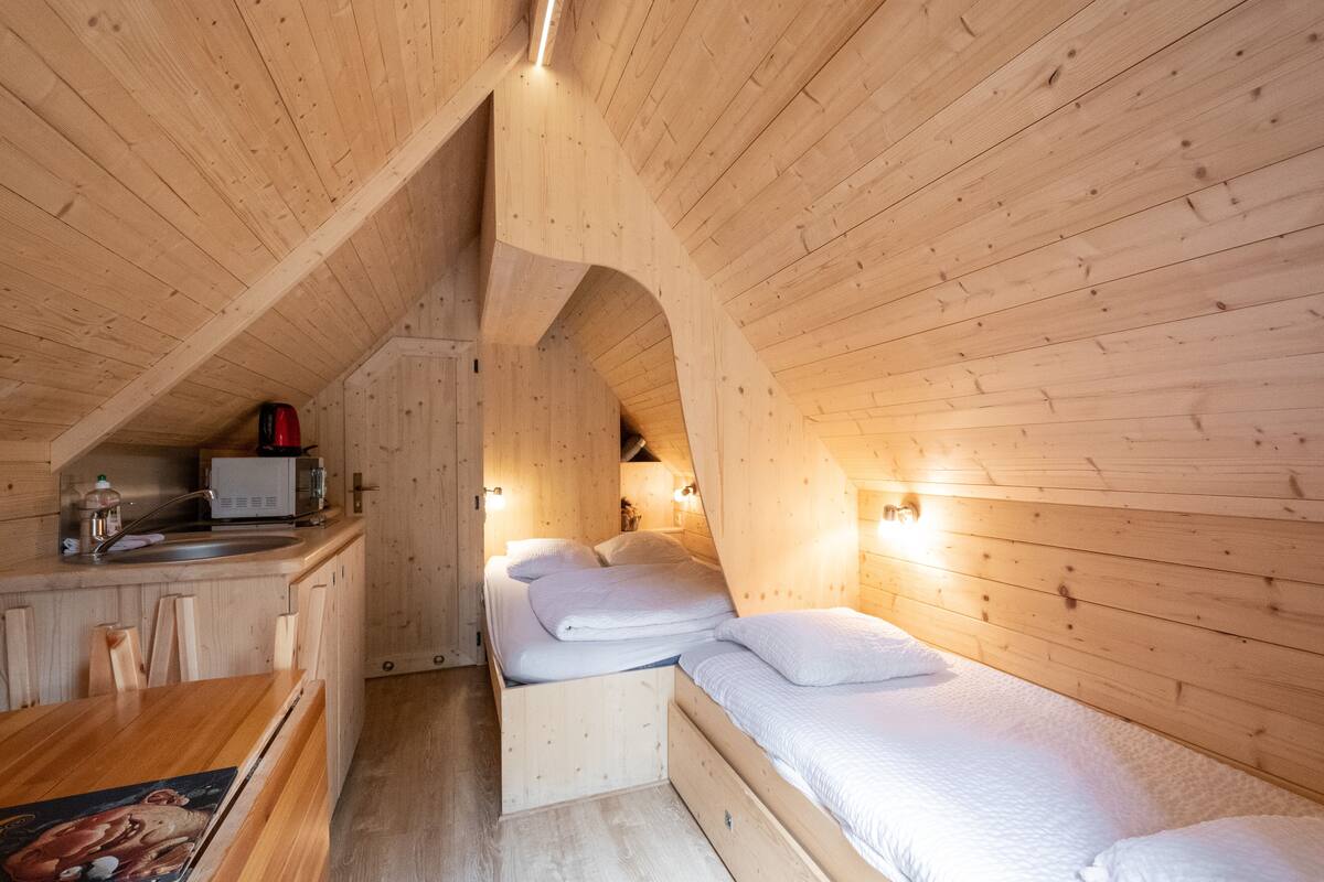 Eine Holzhütte mit Küchenzeile, einem Bett mit weißer Bettwäsche und einem kleinen Esstisch.
