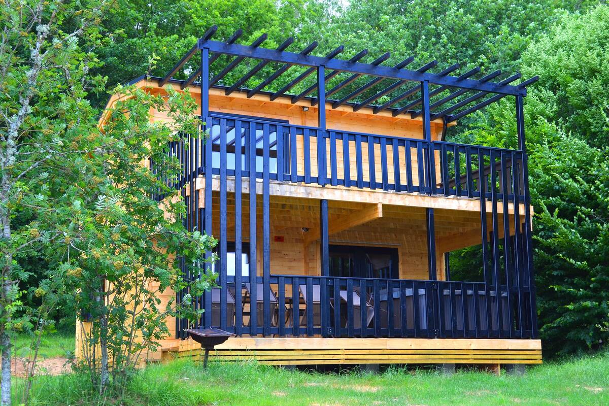 Eine zweistöckige Holzhütte mit einem Balkon, umgeben von Bäumen.