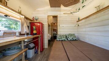A compact kitchen with a red refrigerator, wooden shelves, and a bench.